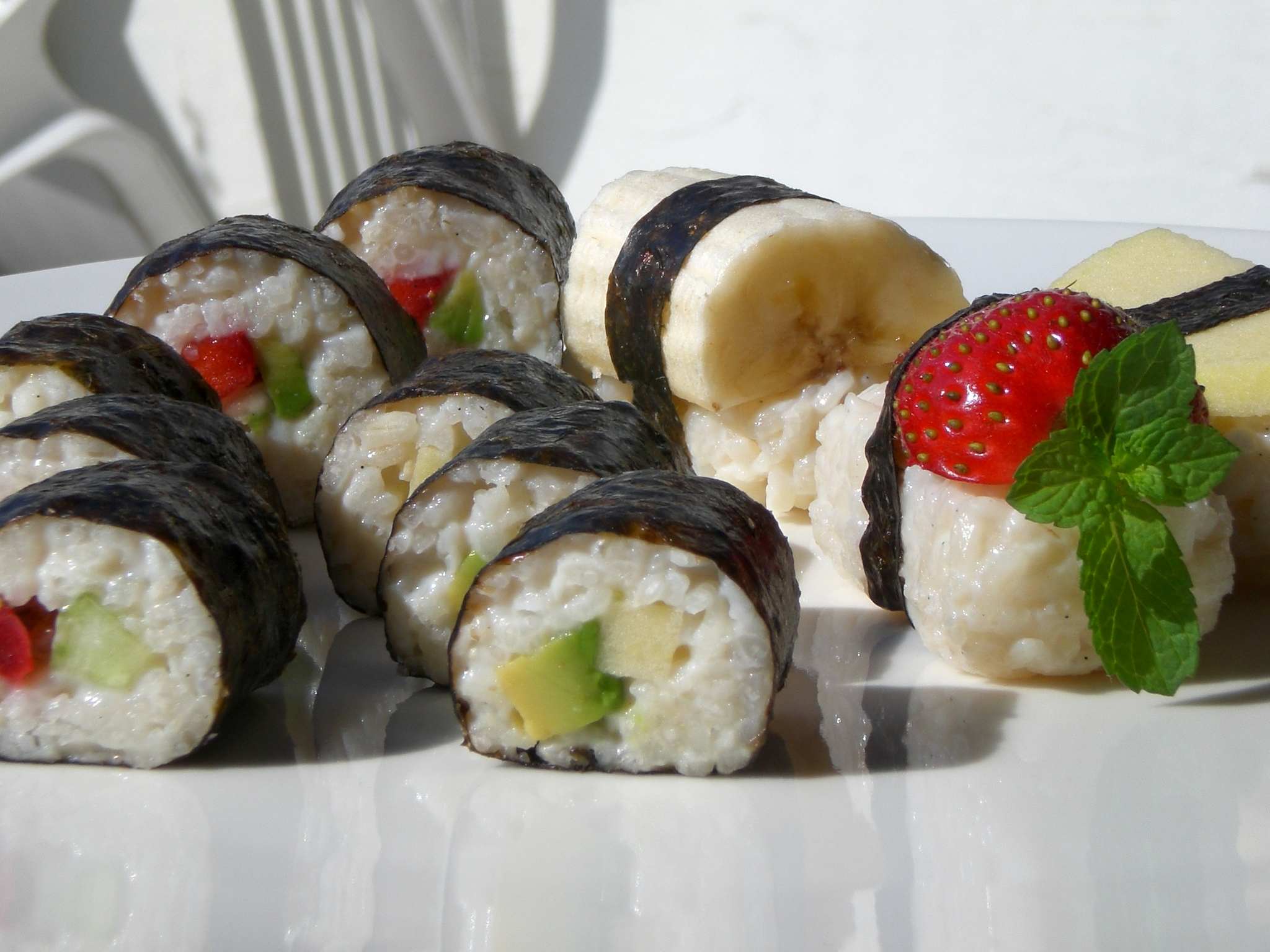 maki sushi on its side with cucumbers, strawberries, and mint leaves inside.