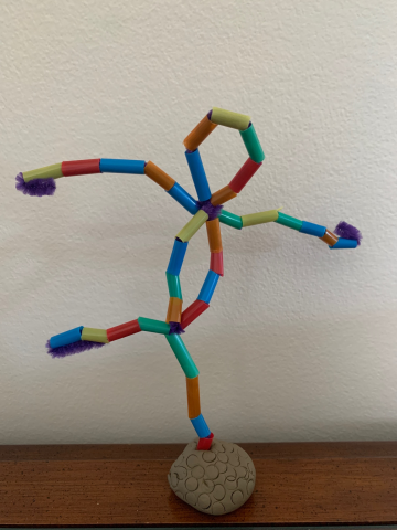 Photograph of a pip cleaner bent into the shape of human with beads all over it and attached to a clay bottom