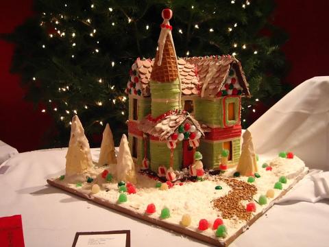 Gingerbread house on a white candy stand with a tag on the bottom left and stars in the background