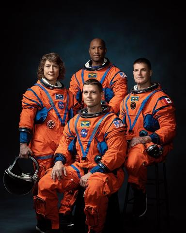 Four astronauts in a circle with orange jumpsuits.