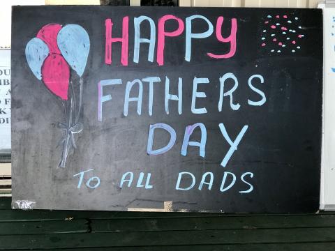 Chalkboard with Happy Fathers Day to All Dads in pink and blue with pink and blue balloons on the left hand side.
