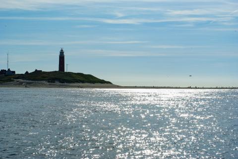 Lighthouse in the top left with sun reflecting off the sea and a blue sky.