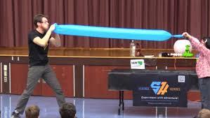 man blowing up large blue balloon with a child assistant