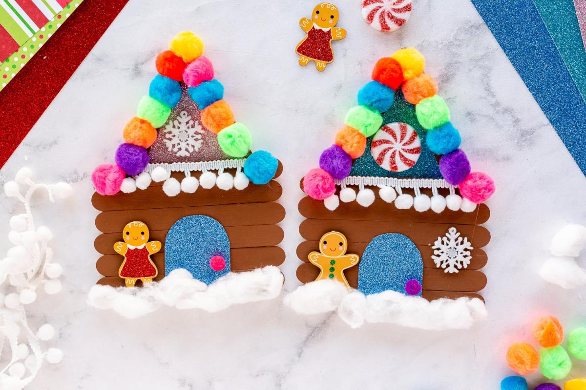 gingerbread houses out of popsicle sticks decorated with stickers and pom poms
